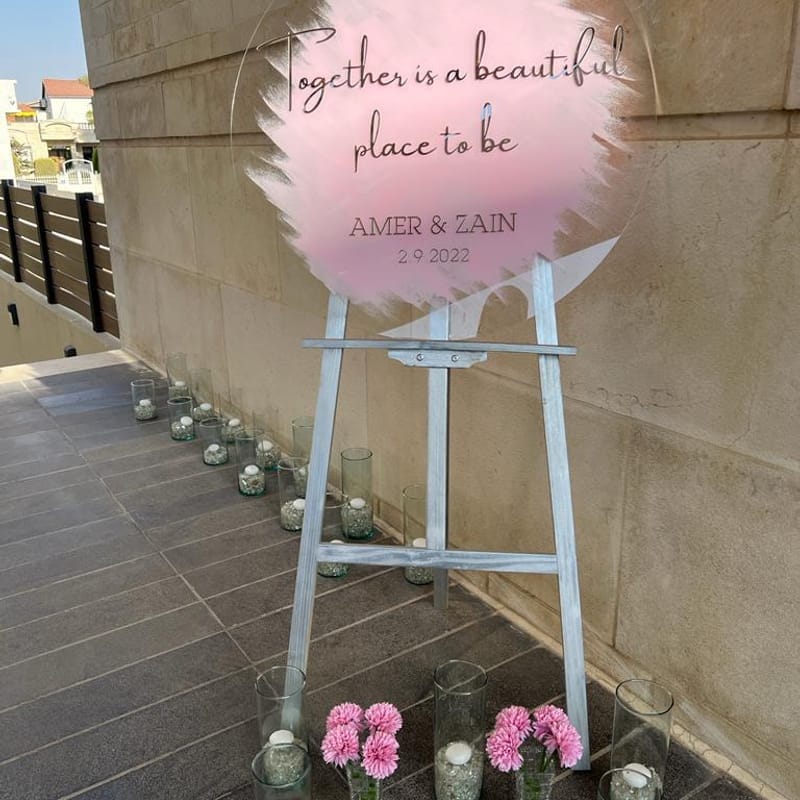 Hand-painted acrylic wedding welcome sign for Amer and Zain on decorative easel with pink flowers