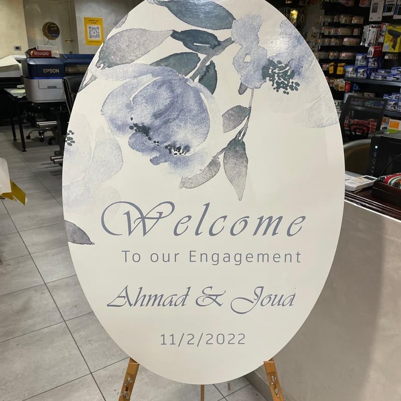 Custom printed oval engagement party welcome sign for Ahmad and Joud with watercolor floral design on easel