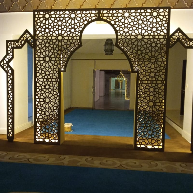 Backlit CNC-cut Islamic geometric archway with side panels installed in a carpeted hall