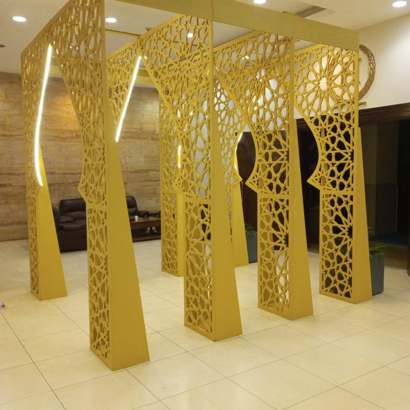 Freestanding gold CNC-cut Islamic geometric arch structure with LED strips in a tiled lobby