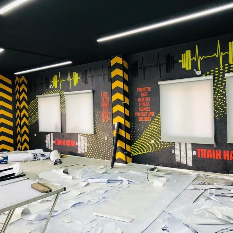 Complete gym interior wall wrap installation with TRAIN HARD motivational graphics, chevron patterns, and heartbeat design