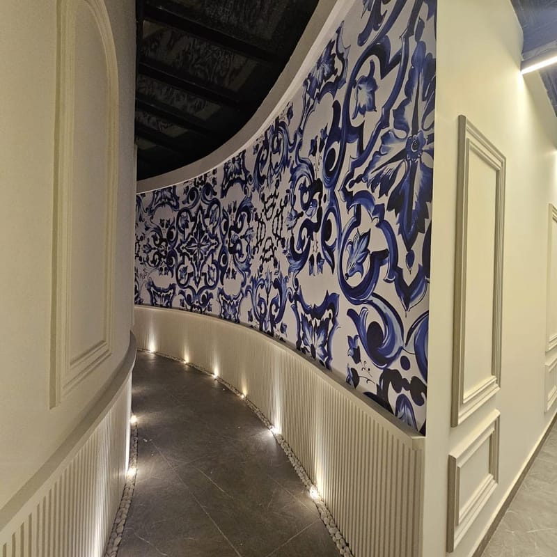 Curved corridor wall covered in a printed blue and white tile pattern mural with floor uplights