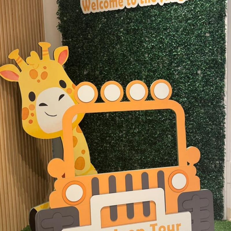 Giraffe and orange safari jeep photo frame cutout in front of a green grass wall