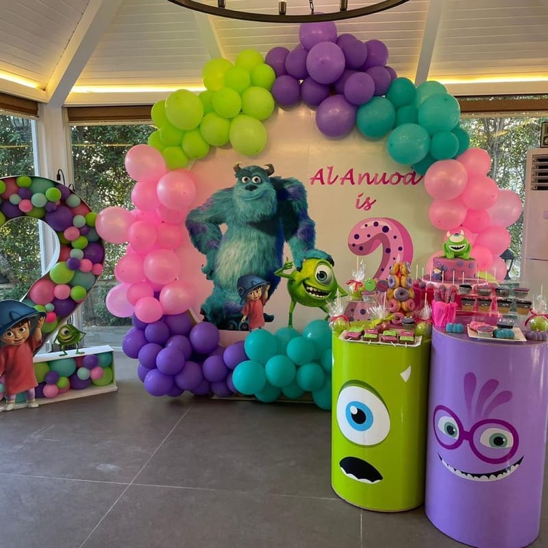 Monsters Inc themed birthday party backdrop with character cutouts and balloon arch