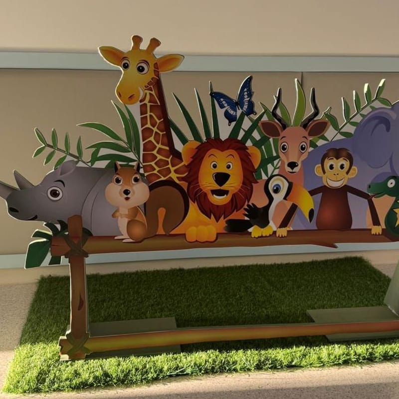 Painted cutout of a giraffe, lion, rhino, monkey and other jungle animals standing on artificial grass