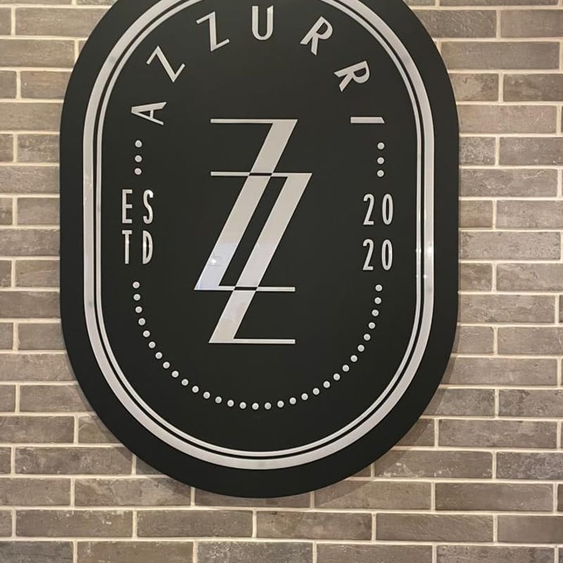 Custom oval acrylic indoor restaurant sign for Azzurri mounted on exposed brick wall