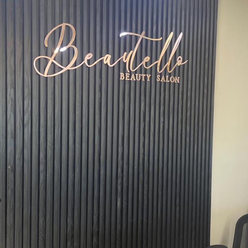 Elegant rose gold dimensional lettering reception sign for Beautello Beauty Salon on dark ribbed feature wall